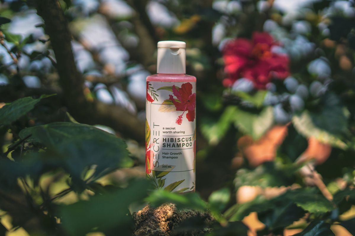 A dry shampoo bottle standing among green leaves