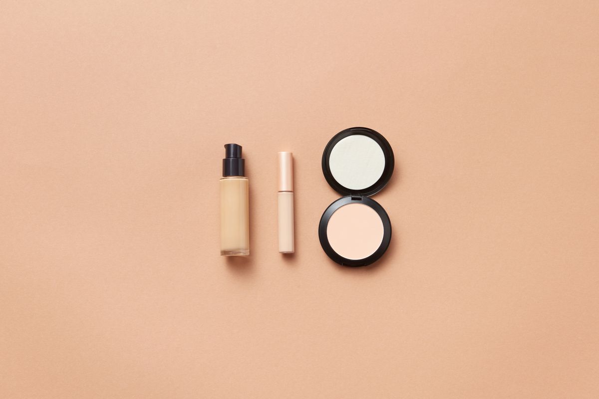 Three liquid foundation bottles lined up beside a makeup brush on a vanity