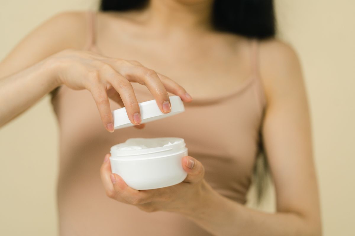 Hands opening a small cosmetic container of cream