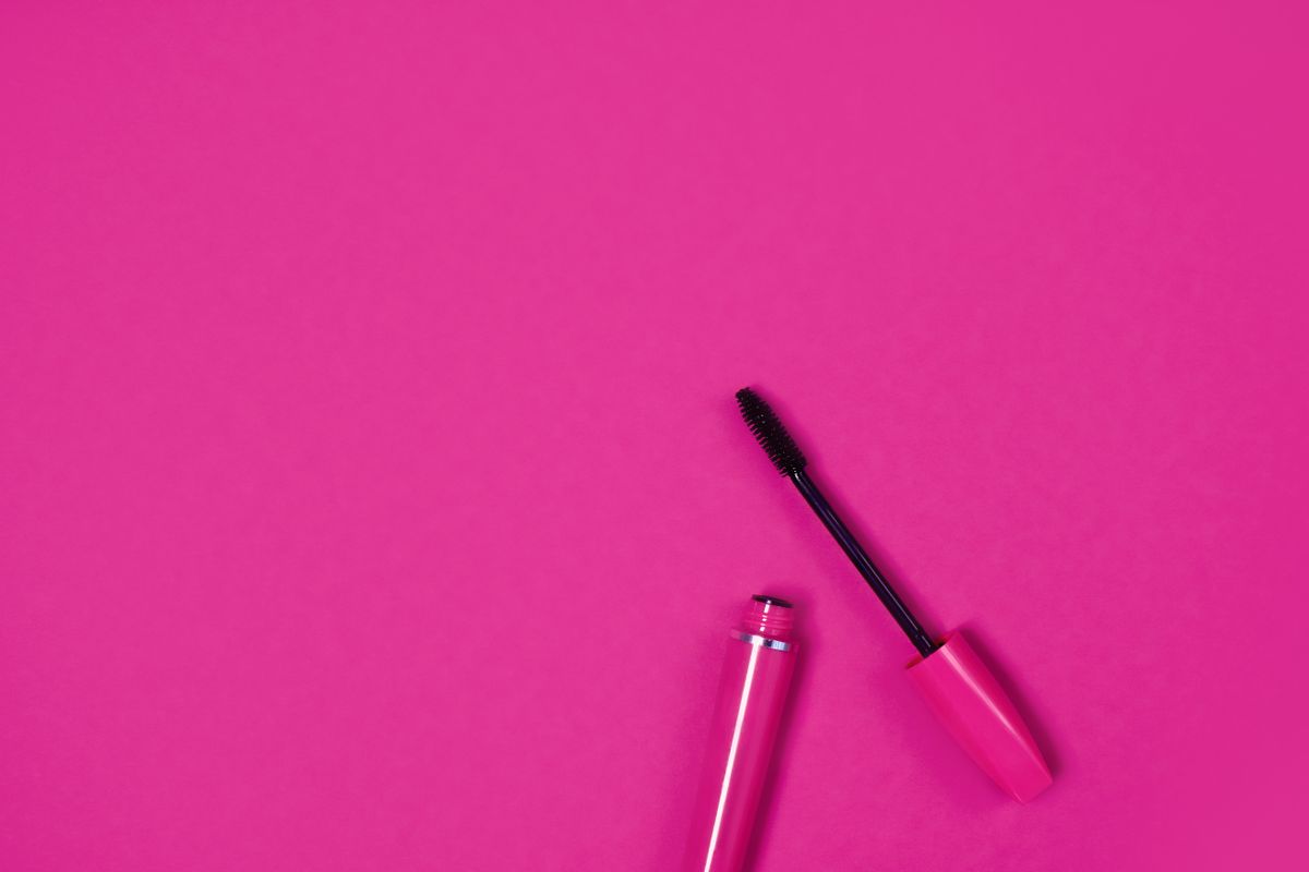 Two mascara tubes standing open with a wand in front of a mirror