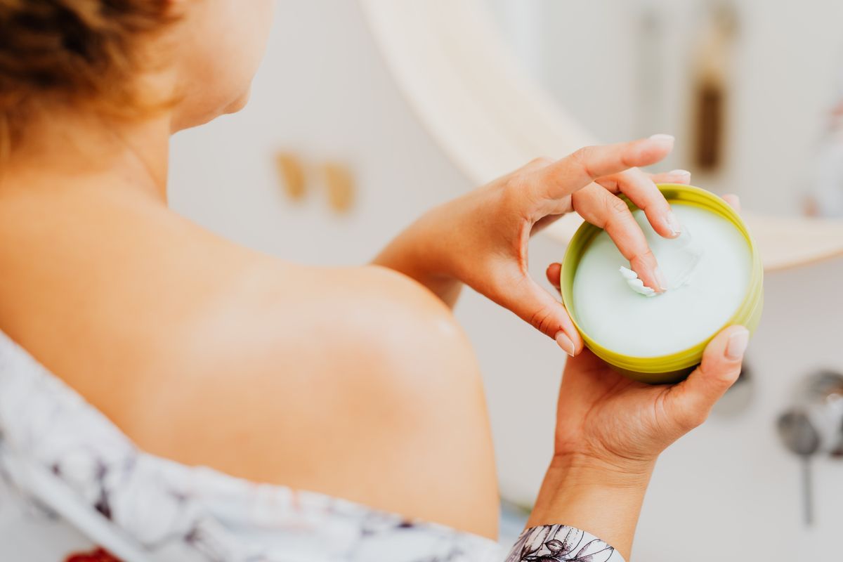 Woman applying face cream in a warm-lit bathroom